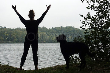 Walkmuehle  Deutschland  Silhouette  Frau macht in Begleitung ihres Hundes an einem See Gymnastik