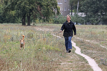 Neuenhagen  Deutschland  Frau geht lachend mit ihrem Hund spazieren