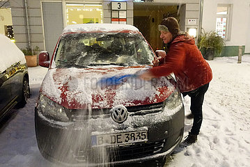 Berlin  Deutschland  Mann fegt am Abend den frisch gefallenen Schnee von seinem geparkten Auto