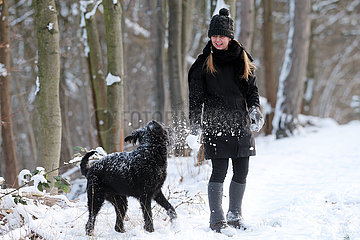 Berlin  Deutschland  Frau spielt im Winter bei Schnee mit ihrem Hund