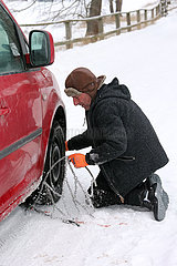 Graditz  Deutschland  Mann zieht im Winter eine Schneekette auf einen Vorderreifen seines Autos