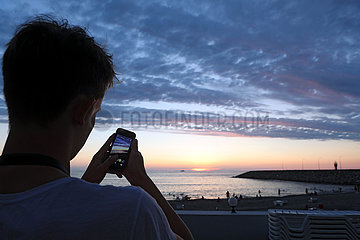 Batumi  Georgien  Junge fotografiert den Sonnenuntergang an der Strandpromenade mit seinem Smartphone