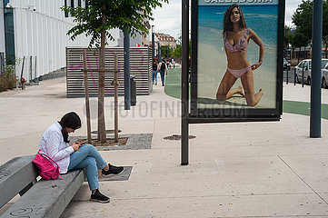 Lissabon  Portugal  Junge Frau sitzt neben einem Werbeplakat und schaut auf ihr Handy