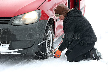 Graditz  Deutschland  Mann zieht im Winter eine Schneekette auf einen Vorderreifen seines Autos