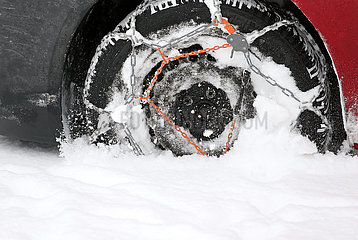 Graditz  Deutschland  Autoreifen mit aufgezogener Schneekette faehrt durch tiefen Schnee