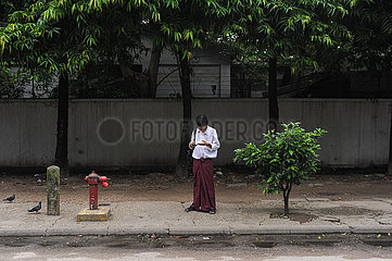 Yangon  Myanmar  Ein Mann steht am Strassenrand und starrt auf sein Handy