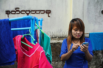 Yangon  Myanmar  Junge Frau mit Smartphone steht neben einem Waeschestaender