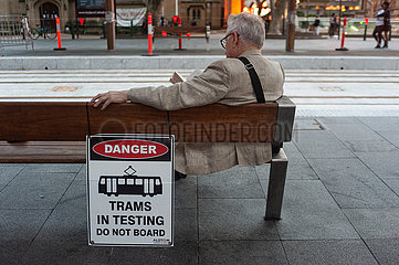 Sydney  Australien  Mann sitzt auf der Bank einer Strassenbahnhaltestelle und liest ein Buch