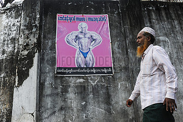 Yangon  Myanmar  Muslimischer Mann geht an einer Wand mit einem Bodybuilding-Poster vorbei