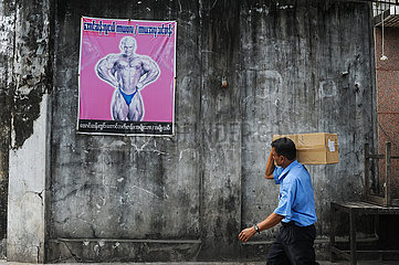 Yangon  Myanmar  Paketbote traegt ein Paeckchen und geht an einer Wand mit einem Bodybuilding-Poster vorbei