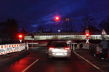 Berlin  Deutschland  Menschen und Auto warten am Abend an einem Bahnuebergang auf die Durchfahrt einer S-Bahn der Linie 2