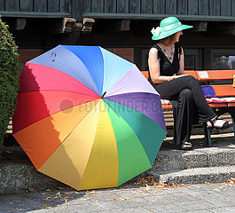 Dresden  Deutschland  Frau mit Sonnenhut sitzt neben einem Schirm in Regenbogenfarben