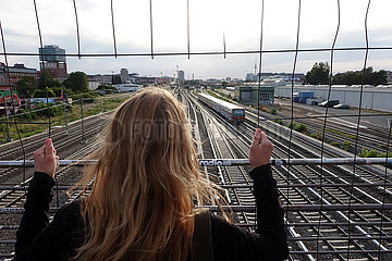 Berlin  Deutschland  Frau schaut durch ein Gitter auf Bahngleise
