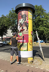 Berlin  Deutschland  Mann klebt ein neues Werbeplakat an eine Litfasssaeule