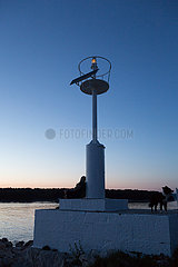 Kroatien  Krk (Hauptstadt der Insel Krk) - Mann mit Hund am Leuchtturm des Yachthafens geniesst die Abenddaemmerung