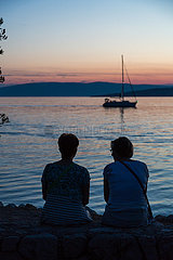 Kroatien  Krk (Hauptstadt der Insel Krk) - Zwei Frauen am Strand geniessen die Abenddaemmerung mit Blick auf die Bucht vor Krk
