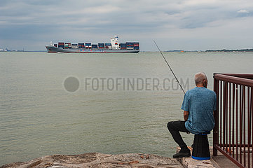 Singapur  Republik Singapur  Mann angelt am Ufer des Changi Beach Parks waehrend ein Frachtschiff vorbeifaehrt