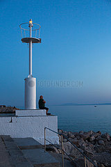 Kroatien  Krk (Hauptstadt der Insel Krk) - Mann am Leuchtturm des Yachthafens geniesst die Abenddaemmerung