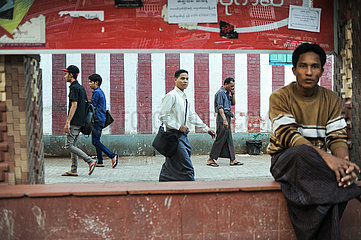 Yangon  Myanmar  Mann wartet an einer Bushaltestelle waehrend im Hintergrund Menschen vorbeigehen