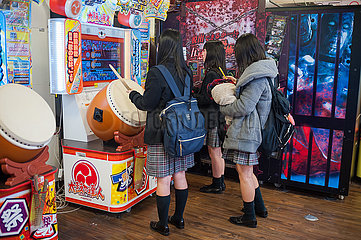 Kyoto  Japan  Schuelerinnen in Schuluniform stehen vor einem Spielautomaten und spielen ein Taiko Trommelspiel