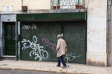 Lissabon  Portugal  Aelterer Mann mit Kruecke geht in der Altstadt eine Strasse entlang