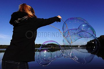 Dranse  Deutschland  Frau macht an einem See mit einem Seil grosse Seifenblasen