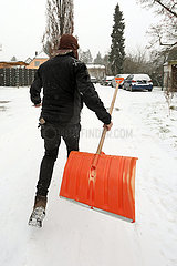 Berlin  Deutschland  Mann laeuft mit Schneeschaufel in der Hand einen Fussweg entlang