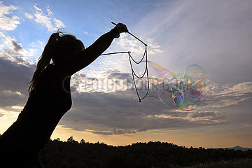 Capodimonte  Italien  Silhouette: Frau macht bei Daemmerung mit einem Seil grosse Seifenblasen