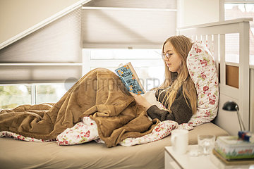 Junge Frau liest an einem kalten Wintertag zuhause im Bett ein Buch  München  9. Januar 2022