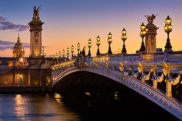 Frankreich  Paris (75) (7. Arrondissement). Pont Alexandre III Brücke und beleuchtete Lampenpfosten bei Sonnenuntergang mit Blick auf die Invalides