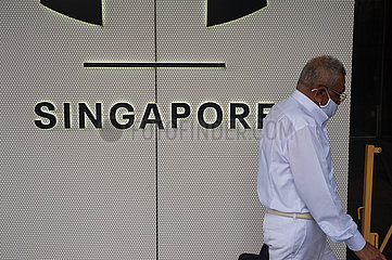 Singapur  Republik Singapur  Mann mit Corona-Mundschutz geht an einem Schriftzug mit der Aufschrift Singapore vorbei