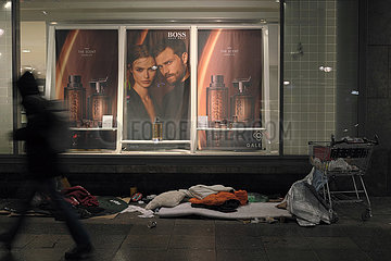Deutschland  Berlin - Utensilien von Obdachlosen vor Schaufenster von Karstadt mit Werbefoto fuer Parfuem der Edelmarke Boss