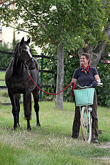 Gestuet Westerberg  Frau auf einem Fahrrad haelt ein Pferd am Fuehrstrick