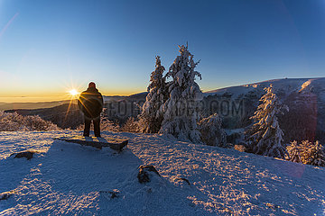 FRANCE  Alsace  Haut-Rhin (68)  Ballons des Vosges Regional Nature Park  Hiker at Trois Fours in winter watching the sunrise