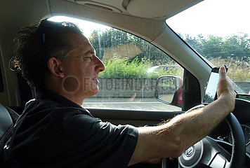Berka  Deutschland  Mann schaut waehrend einer Autofahrt auf sein Mobiltelefon