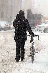 Berlin  Deutschland  Frau schiebt bei heftigem Schneefall auf einer Strasse ihr Fahrrad