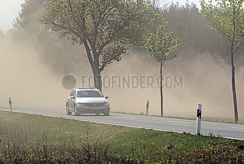 Doebrichau  Deutschland  Auto faehrt auf einer Landstrasse durch eine bei der Feldarbeit entstandene Staubwolke