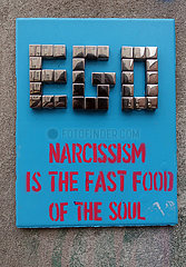 Krakau  Polen  Street-Art: Steinplatte mit der Aufschrift EGO Narcissism is the Fast Food of the Soul haengt an einer Hauswand