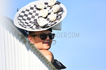 Iffezheim  Deutschland  elegant gekleidete Frau mit Hut schaut ueber einen Zaun