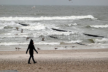 Ustka  Polen  Frau geht allein am Strand der stuermischen Ostsee spazieren