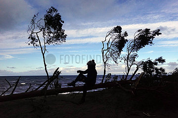 Ustka  Polen  Silhouette: Frau sitzt am Strand auf einem umgestuerzten Baum