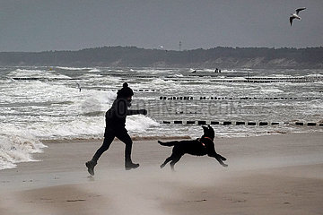 Ustka  Polen  Frau geht mit ihrem Hund am Strand der stuermischen Ostsee spazieren