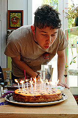 Berlin  Deutschland  junger Mann blaest die Kerzen auf seinem Geburtstagskuchen aus