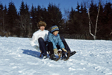 Frauenwald  Deutsche Demokratische Republik  Mutter und Sohn fahren auf einem Schlitten einen verschneiten Huegel herunter