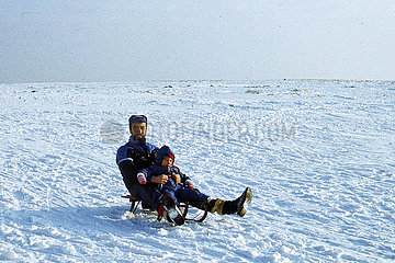 Frauenwald  Deutsche Demokratische Republik  Vater und Sohn fahren auf einem Schlitten einen verschneiten Huegel herunter