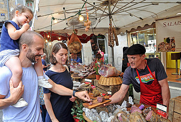FRANCE. LOT (46) FIGEAC MARKET. A YOUNG COUPLE WITH THEIR CHILD TASTE REGIONAL CHARCUTERIE SPECIALTIES