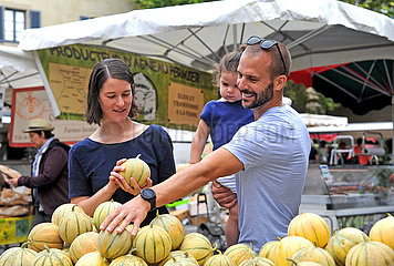 FRANCE. OCCITANY. LOT (46) FIGEAC MARKET. A YOUNG COUPLE AND THEIR CHILD CHOOSING A LOCAL MELON