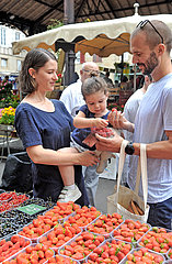 FRANCE. OCCITANY. LOT (46) FIGEAC MARKET. A YOUNG COUPLE WITH THEIR CHILD  IN FRONT OF A FRUIT STAND
