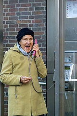 Deutschland  Bremen - Ruestige Rentnerin telefoniert an einer Telefonzelle der Deutschen Telekom
