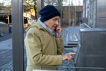 Deutschland  Bremen - Ruestige Rentnerin waehlt eine Nummer an einer Telefonzelle der Deutschen Telekom